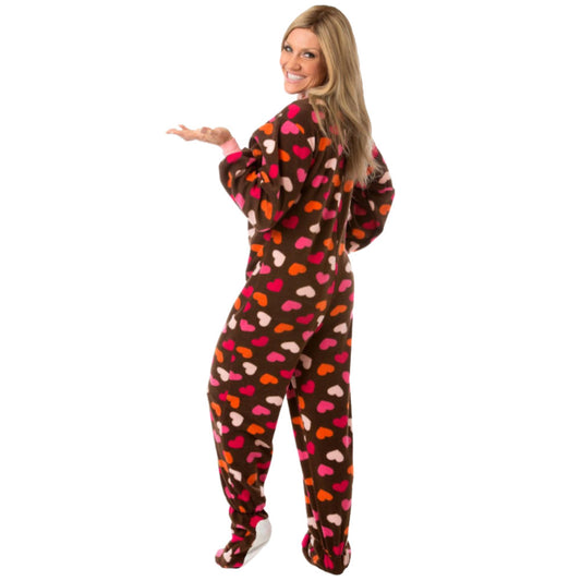 An attractive blond woman smiling wearing Chocolate Brown Fleece Onesie Footed Pajamas that have many Pink, White, and Orange Hearts all over them from Big Feet Pajama Company