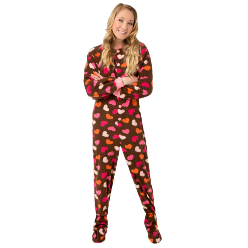 A young blond woman, in her teens smiling modeling Chocolate Brown Fleece Onesie Footed Pajama that has Pink, White, and Orange Hearts all over them, from Big Feet Pajamas.