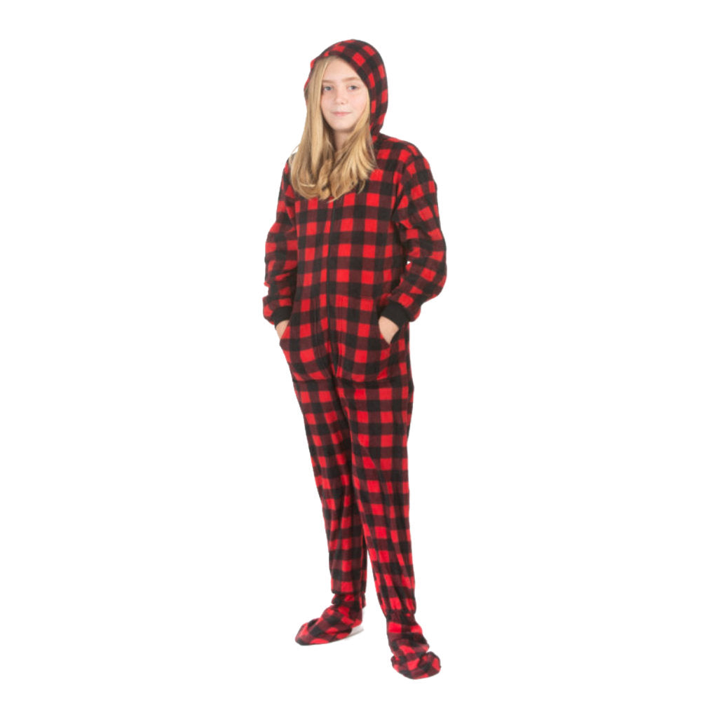 A girl is wearing hoodie footie pjs from the Big Feet Pajama Company line of warm fleece footed onesies that make getting ready for bed and relaxing at home fun. This outfit is made of fleece, with the pattern being in Red and Black Buffalo plaid. She has her hood on and her hands in the pockets.