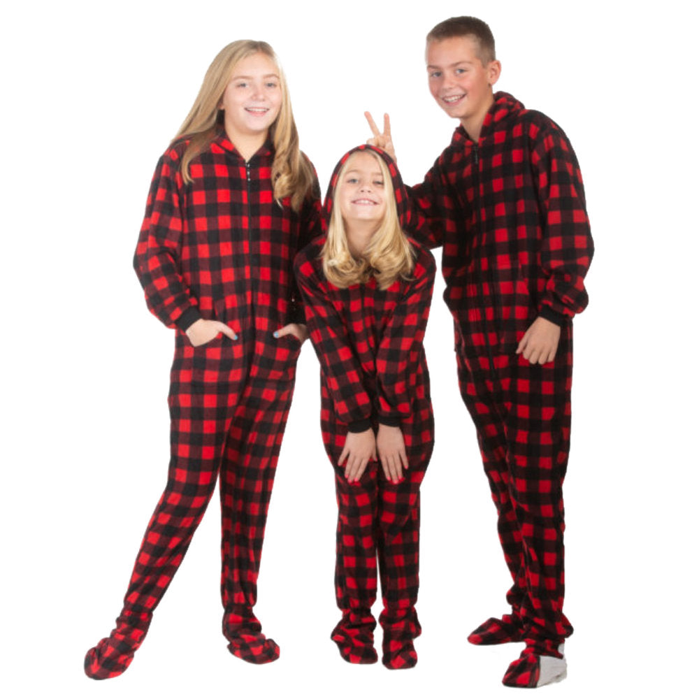Brother and his two sisters are posing for Christmas pictures wearing red & black buffalo plaid fleece hoodie-footed onesie pajamas from the Big Feet Pajama Company. The girls have the hood on or hands in the kangaroo pockets. The brother is holding 2 fingers, "bunny ears" or maybe "devil horns" over is little sisters head.