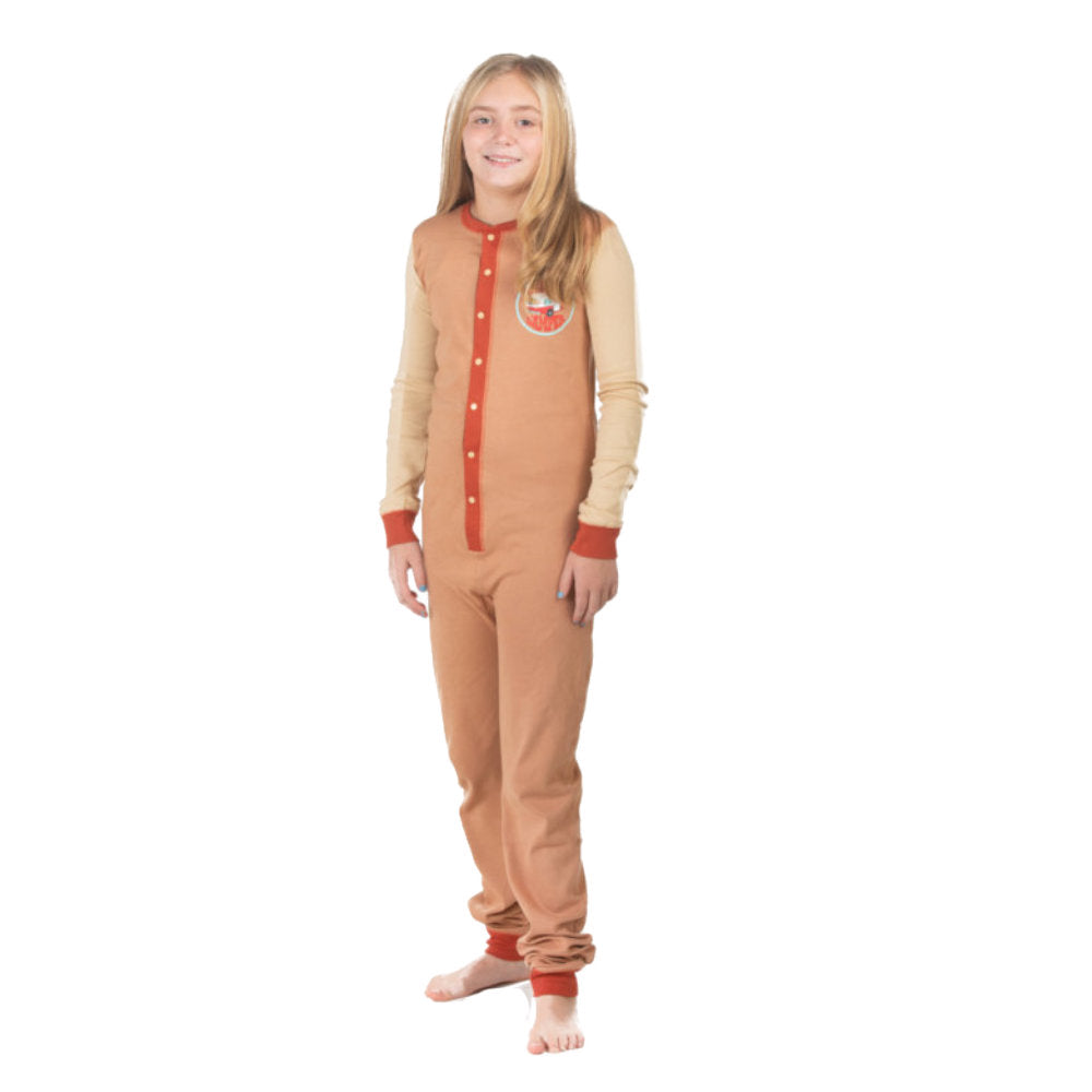 A girl wearing a brown and beige onesie from the Big Feet Pajama collection of 100% cotton Union Suit Sleepwear and Playwear. The onesies feature a "Happy Camper" badge on the chest. The onesies have long sleeves, cuffs, a snap-up front, and a decorative rear flap with the Happy Camper Bear and Moose by the fire at their campsite.