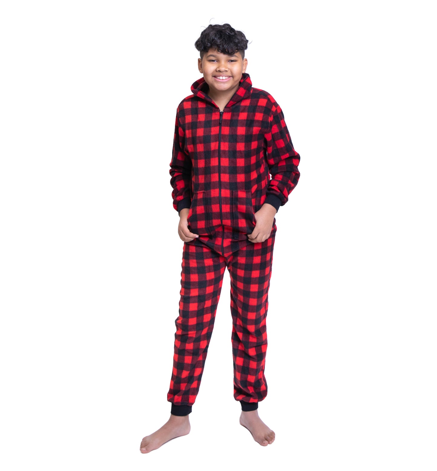 A teen boy is wearing hoodie jumpsuit pjs from the Big Feet Pajama Company line of matching family onesies pajamas. This one-piece outfit is footless and a Christmas favorite made of Red and Black Buffalo plaid micro-polar fleece.