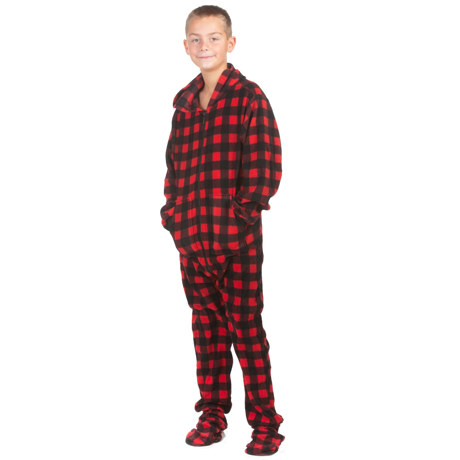 A boy is wearing one-piece pjs from the Big Feet Pajama Company line of fleece footed onesies. It is red & black buffalo plaid fleece with a hood and kangaroo pockets.
